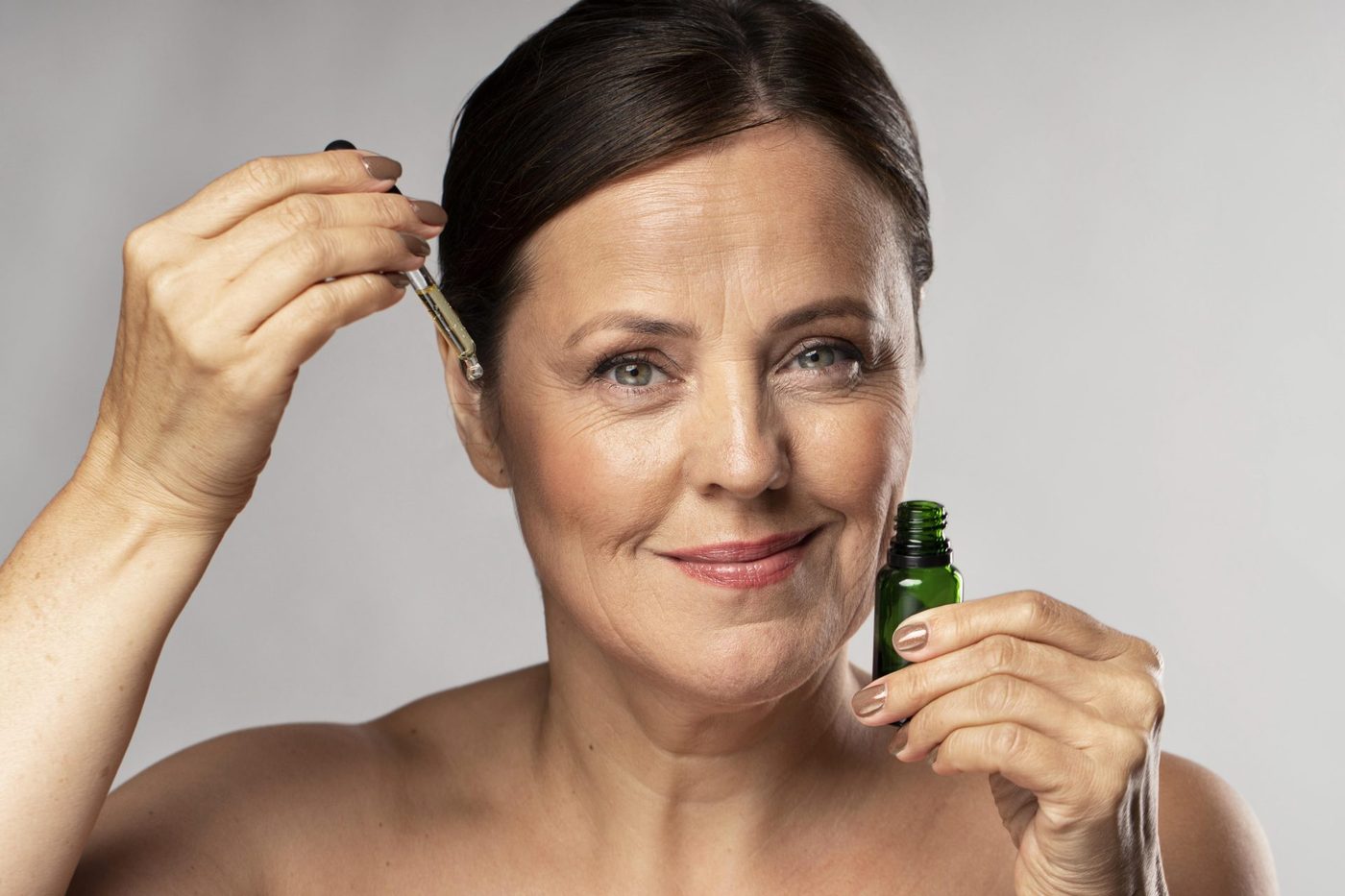 Femme appliquant quelques gouttes d'huile sur son visage, en souriant