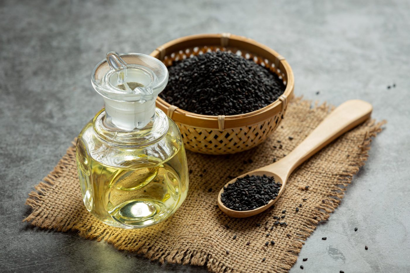 Graines de nigelle dans une coupelle tressée, à côté d'une carafe d'huile